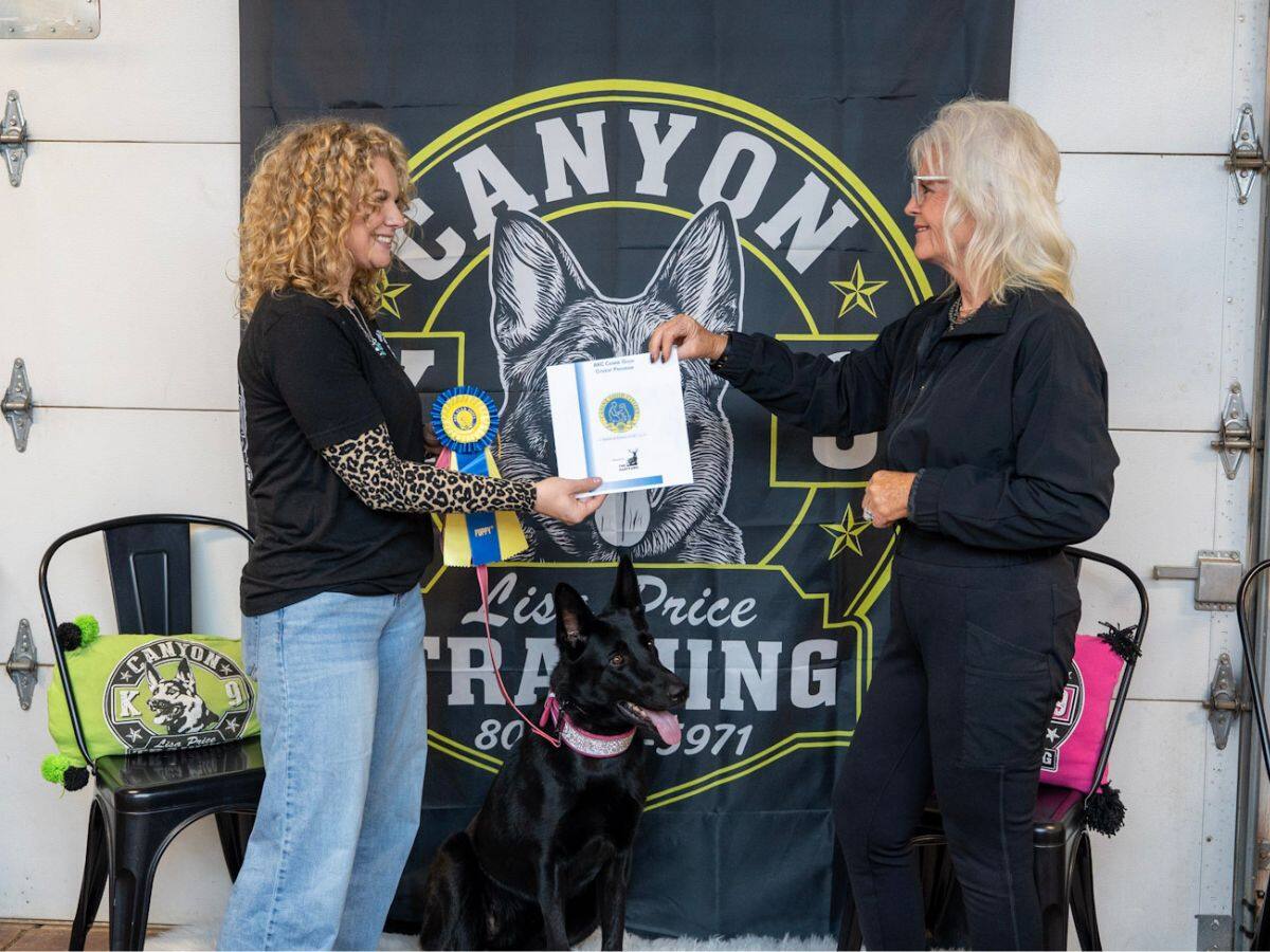 Lisa Price and another woman holding a certificate and ribbon beside a black shepherd